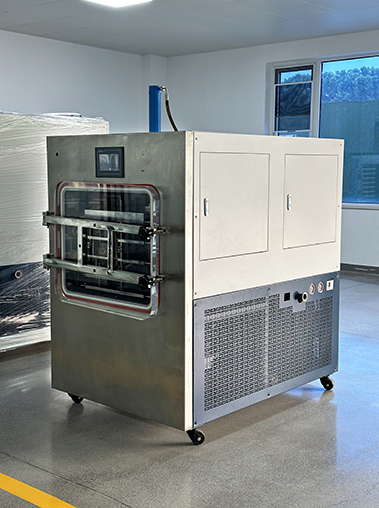 Three-quarter right view real shot of a commercial freeze dryer machine on wheels, featuring dual service doors on the upper white cabinet and pressure gauges near the bottom blue grille.